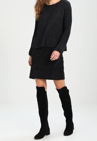 Svart ribbad tröja med långa ärmar, parat med en svart mockaskirt och svarta mocka stövlar över knäet. Texturerade tygdetaljer synliga.