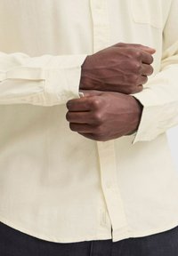 Camisa abotonada de un amarillo claro con un bolsillo, que presenta mangas largas y botones de contraste. La tela parece suave con un ligero brillo.