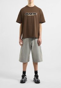 Brązowy bawełniany T-shirt z logo "AVAX AIVREX DEPT.", parowany z paskowanymi szortami dżinsowymi i czarnymi butami sportowymi z szarymi akcentami.