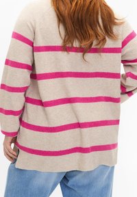 Pull beige à rayures roses, texture côtelée, coupe oversize et manches longues. Comprend des fentes latérales et un ourlet détendu.