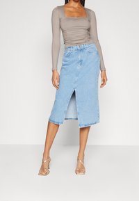 Ljusblå jeanskjol med en framåtslits, midjefånget längd och klassisk design med fem fickor. Matchas med en figurnära, rynkad långärmad topp.