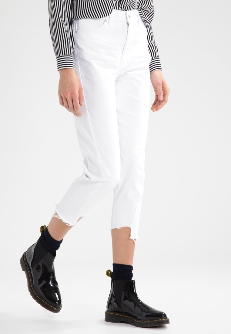 Valkoiset lyhyet farkut, joissa on repaleiset lahkeet, yhdistettyinä kiiltävän mustiin nilkkabootseihin. Asusteena on mustavalkoruudullinen pitkähihais shirt.