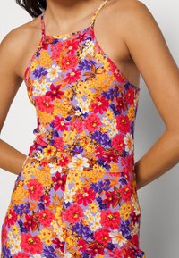 Vestido ajustado con estampado floral y tirantes finos. Presenta colores vibrantes: flores rojas, moradas, naranjas y blancas sobre un fondo lila.