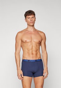 Boxeri scurți bleu marin cu un tiv lat, având un logo "PUMA" albastru. Realizați dintr-un material moale, oferind un design ajustat și fără modele.