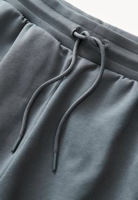 Szare spodenki sportowe wykonane z miękkiego materiału, z elastycznym paskiem w talii z sznurkiem do regulacji oraz gładką, teksturowaną powierzchnią bez wzorów.
