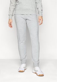 Graue Baumwoll-Jogginghosen mit einer schmalen Passform, elastischen Bündchen und einer glatten Textur. Kombiniert mit weißen Sneakers mit hellgrauen Akzenten.