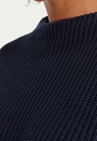 Granatowy sweter dziany z teksturowanym wzorem prążkowanym i wysokim kołnierzem, prezentujący zbliżenie na splot tkaniny.