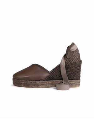 Zapato espadrille marrón con cuña, tacón trenzado, puntera cerrada y cinta para atar al tobillo sobre fondo blanco.