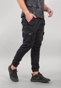 Mustat kuormahousut, joissa on useita taskuja, kapeaksi kapeneva malli ja joustavat resorit, valmistettu kevyestä, sileäpintaisesta kankaasta.