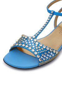 Sandalo blu con suola piatta, impreziosito da vari strass trasparenti e un elegante accento dorato. Texture in pelle liscia.