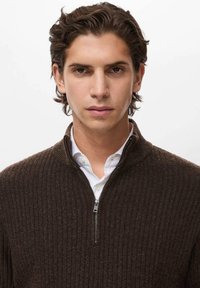 Pullover marrone a coste con colletto a zip a un quarto e zip argentata. Indossato sopra una camicia bianca con colletto, che mette in mostra un design a maglia testurizzato.
