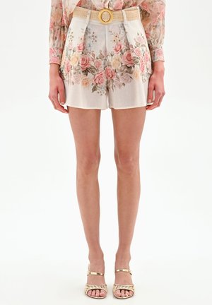 Shorts a vita alta con fantasia floreale, cintura intrecciata e fibbia circolare, indossati con una camicetta a maniche lunghe floreale abbinata e tacchi dorati con cinturini.