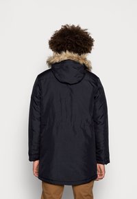 Marinblå parka med huva i fauxpäls, långa ärmar och en avslappnad passform. Har en jämn yta och en detalj med bakventil.