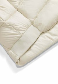 Licht beige geweven dekbed met een gladde, luchtige textuur. Heeft een zachte, gebreide rand aan de onderkant.