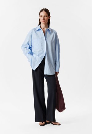 Light blue striped shirt with a pocket, oversized fit, paired with black wide-leg pants and brown tote bag, flat sandals.
