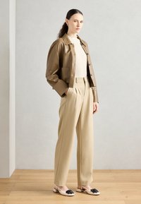 Brown leather cropped jacket, cream ribbed sweater, beige pleated trousers, white shoes with black accent. Smooth texture, tailored fit.