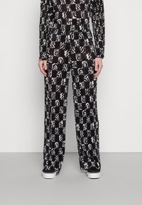 Calças largas de padrão preto e branco com textura plissada, apresentando desenhos abstractos e uma cinta elástica confortável.