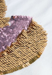 Rosa und goldene Pailletten sind kreisförmig auf einem weißen Stoff angeordnet und zeigen eine glänzende, strukturierte Oberfläche mit überlappenden Scheibenformen.