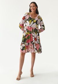 Blumenmuster Kleid mit langen Ärmeln, einem V-Ausschnitt und gestuften Rüschen. Die Farben umfassen Pink, Weiß, Grün und Schwarz, mit auffälligen Blumenmustern.