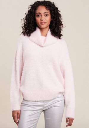 Hellrosa, flauschiger Pullover mit einem hohen, umgeschlagenen Kragen und langen Ärmeln. Tragen mit glänzenden silbernen Hosen. Glatte Textur, lockere Passform.