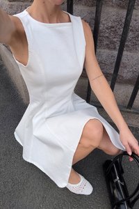Abito bianco senza maniche con orlo svasato, realizzato in un materiale morbido. Abbinato a una borsa nera e scarpe bianche con texture.