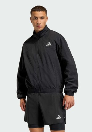 Čierny vetrovka na zips s vysokým golierom, s reflexným logom na hrudi. Ľahká tkanina s elastickými manžetami a pásom.