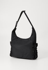 Sac à épaule en tissu noir avec une forme arrondie, une bandoulière ajustable et des détails froncés sur les côtés. Texture lisse et apparence douce.