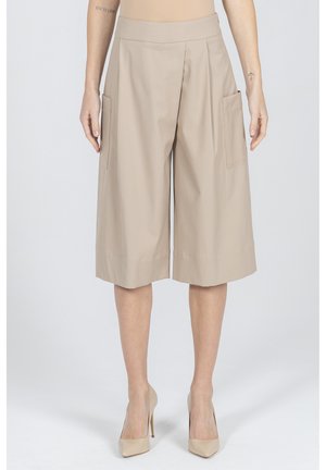 Beżowe szerokie spodenki do kolan z dużymi bocznymi kieszeniami, noszone z beżowymi szpilkami, na stojącej osobie.