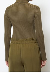 Olivově zelený žebrovaný rolák s přiléhavými dlouhými rukávy, spárovaný s odpovídajícími kalhotami s vysokým pasem a nashromážděným pasem.