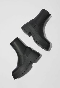 Mustat nilkkurit, jotka on valmistettu sileästä nahasta. Niissä on paksu kumipohja, jossa on syvät urat, ja hyvin istuva varsi.