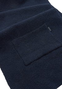 Granatowy dziergany koc z teksturowaną powierzchnią i dużą naszywaną kieszenią. Metka widoczna z jednej strony. Miękki, ciepły materiał.