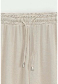 Pantalons de jogging beiges avec une taille élastique, dotés d'un cordon de serrage avec des embouts en métal argenté et d'un tissu texturé.