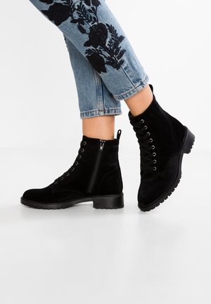 Black suede ankle boots with side zipper and laces worn with light blue jeans featuring black floral embroidery.