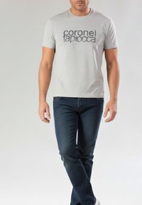 Camiseta de manga corta gris con texto negro que dice "coronel tapiocca" en el frente, combinada con vaqueros azul oscuro. Diseño simple y casual.