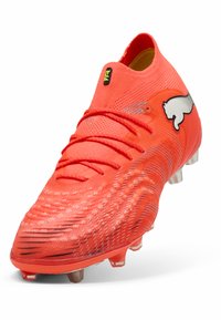 Kirkkaanpunainen jalkapallokenkä, jossa on teksturoitu pinta, kirjotut nauhat ja valkoinen logo. Kenkä on matalavartinen ja siinä on muotoillut pystykiilat pitoa varten.