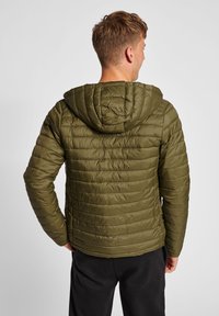 Olivgrön puffy jacka med ett kviltat mönster, fastsydd huva och långärmade ärmar. Materialet verkar glatt och lättvikts.