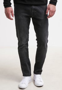 Mustad slim-fit teksad, millel on sile tekstuur, viie tasku disain ja peen tuhmumine, sobitunud valgete spordijalanõudega.