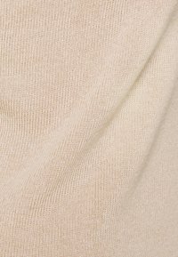 Tejido de punto color beige claro con una textura acanalada, que presenta una sensación suave y ligeramente elástica, con sutiles variaciones de color a lo largo.