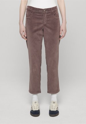 Pantalon droit en velours côtelé marron porté avec des chaussettes blanches montantes et des baskets Adidas noires et blanches.