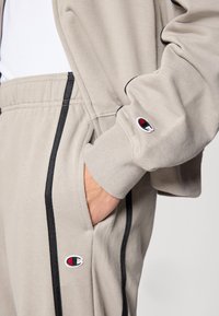 Ανοιχτό γκρι φούτερ με μαύρες λε πτομέρειες, που διαθέτει πλαϊνή τσέπη και κεντημένο λογότυπο στο μανίκι. Μαλακό ύφασμα με ριμπ μανσέτες.