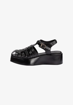 Black leather platform sandal with woven straps, ankle buckle, and closed toe on solid thick sole.