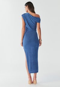 Zila vienas pleca kleita, izgatavota no mīksta, faktūrēta auduma. Tai ir sānu šķēlums un pieguloša siluets ar drapērijas detaļām uz pleca.