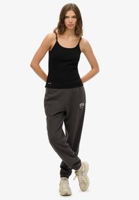 Top ajustado negro sin mangas con tirantes delgados, combinado con pantalones deportivos sueltos gris oscuro que tienen "USA" en blanco. Llevado con zapatillas deportivas beige.