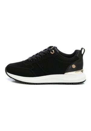 Chaussures de sport noires avec tissu texturé, bout rond, laçage à l'avant et semelle blanche. Présente des accents dorés au niveau du talon et des œillets.