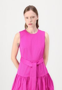 Růžové šaty bez rukávů s přiléhavým korzetem, rozšířenou sukní a zavázaným opaskem v pase. Hladká textura s jemným nařasením na sukni.