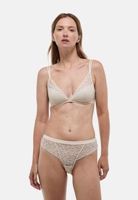 Ensemble de lingerie en dentelle beige comprenant un bralette triangle avec des bretelles réglables et un tanga taille basse assorti avec des détails floraux.