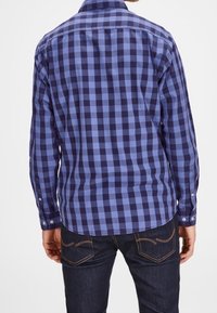 Camisa de botones con un patrón a cuadros en azul y marino, de mangas largas y con un dobladillo curvado. Hecha de una tela con una textura suave.