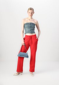 Denim top bez ramienok, červené nohavice so širokými nohavicami a malá modrá kabelka. Model nosí béžové balerínky s detailom mašle; hladké textúry sa kontrastujú.