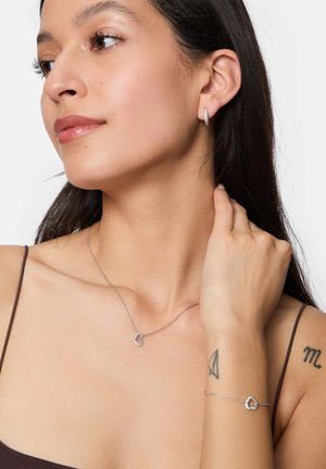 Silbernes Schmuckset mit einer herzförmigen Anhänger-Neklace, passendem Herz-Armband und einfachen Creolen an einem Modell.