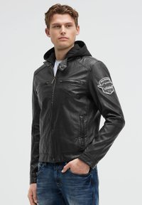 Schwarze Lederjacke mit Kapuze, ausgestattet mit zwei Reißverschluss-Brusttaschen, Seitentaschen und einem Logo-Patch am linken Arm. Klassische Passform.